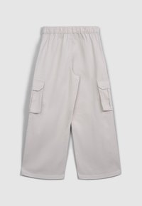Pantalons cargo beige clair avec une ceinture élastique, deux poches latérales et deux poches cargo sur les cuisses. Fabriqués en tissu en coton durable.