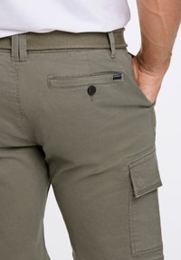 Olivgröna cargobyxor med ett vävt bälte, försedd med en luckficka och en knappstängning på baksidan. Slät, hållbar tygtextur.