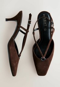 Ruskeat mokkaiset korkokengät, joissa on terävä kärki, ristiin menevät hihnat ja pieni solkikoriste. Pohja on musta ja litteä.