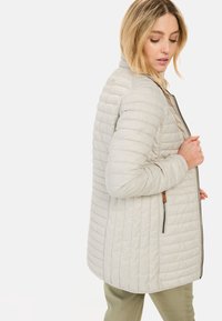 Lichtgrijze gewatteerde jas met een ritssluiting, voorzien van een staande kraag en subtiele textuur. Zijzakken en slim fit.