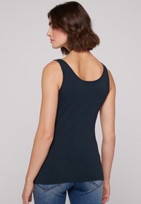 Top sin mangas de un oscuro color navy, hecho de suave algodón, con un escote ovalado y tirantes anchos, ajustado al cuerpo, combinado con unos vaqueros azules.