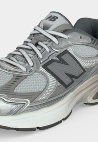 Γκρι και λευκό αθλητικό παπούτσι New Balance με πλέγμα, μαλακή σόλα και κορδόνια μπροστά, εμφανισμένο από πλάγια γωνία.