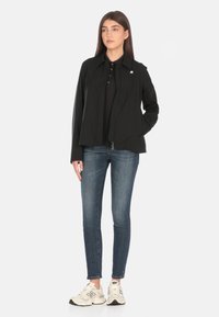 Giubbotto nero con chiusura a zip e colletto, indossato sopra un polo nero, abbinato a jeans blu e sneakers bianche. Tessuto liscia, design minimalista.