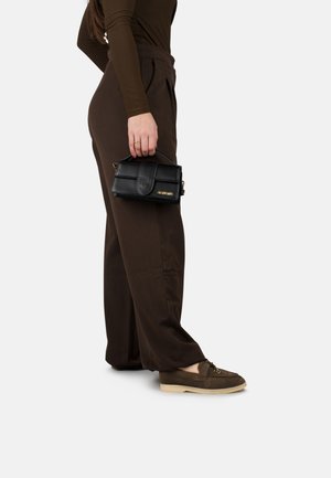 Borsa a tracolla nera in pelle con manico superiore e hardware dorato, abbinata a pantaloni larghi marroni e mocassini marroni con suola chiara.