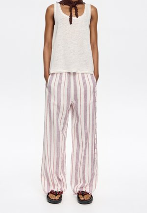 White tank top with a loose fit, paired with red and blue striped wide-leg pants. Pants feature elasticized cuffs and side pockets. Black sandals.
