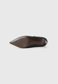Chaussure à talon noir avec un design à bout pointu, texture lisse et semelle en caoutchouc marron. Présente une silhouette élégante et minimaliste.