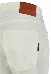 Beige broek met een achterzak, gestikte details en een bruine leren patch met het geperste "HECHTER" logo op de tailleband.