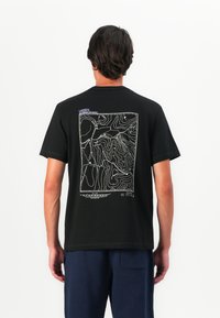 T-shirt noir en coton avec un graphique de carte en contour blanche au dos, avec des accents de texte en violet près de l'encolure. Coupe standard.
