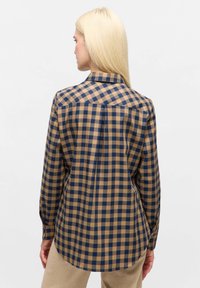 Checkered shirt featuring a tan and navy blue pattern, button-down collar, long sleeves, and curved hem. Fabric appears smooth and lightweight.