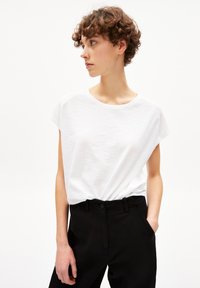 Witte T-shirt met korte mouwen in een relaxte pasvorm, gecombineerd met zwarte op maat gemaakte broek. De stof is soepel met een subtiele textuur.