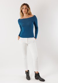 Maglietta azzurra a maniche lunghe con scollatura a spalle scoperte, abbinata a pantaloni bianchi slim e stivaletti neri alla caviglia con tacco basso e zip.