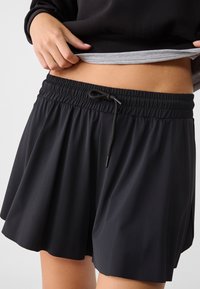 Zwarte sportieve shorts van lichtgewicht stof, met een elastische tailleband en een koord, en een uitlopende silhouet.