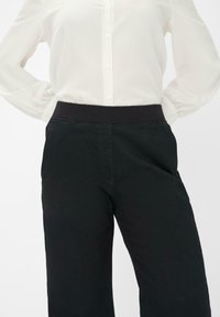 Schwarze Hose mit einem weichen Bund, ausgestattet mit seitlichen Taschen und einem geraden Bein Design. Der Stoff wirkt glatt und leicht dehnbar.