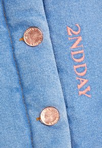 jeansskjorta med ljusblått tyg, rosaguld knappar och broderad "2NDAY" i rosa. Den har en strukturerad krage och sömdetaljer.