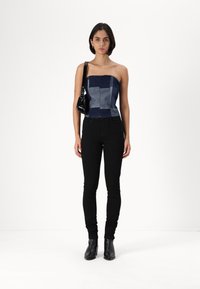 Top fără bretele din denim cu un design patchwork în nuanțe de albastru, purtat cu blugi skinny negri și cizme cu glezna. Geantă de umăr neagră inclusă.