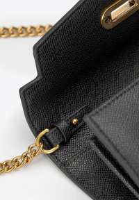 Černá kožená kabelka s texturovaným povrchem, zlatým řetízkovým popruhem a kovovým zapínáním. Vnitřek obsahuje přihrádky a hladkou podšívku.