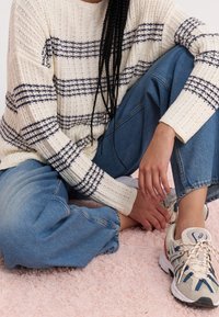 Maglione girocollo color crema con righe blu navy, tessuto a maglia. Pantaloni larghi in denim blu. Scarpe da ginnastica di colore chiaro con dettagli in mesh.