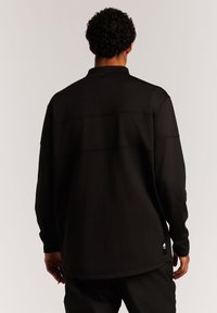 Schwarzes Langarmshirt aus glattem Stoff, mit hohem Kragen, lockerer Passform und dezenten Nähten auf dem Rücken.