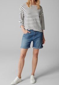 Camisa de manga larga ligera a rayas en crema y azul marino. Short de mezclilla de tiro alto y enrollados en azul claro. Zapatillas blancas con suelas texturizadas.