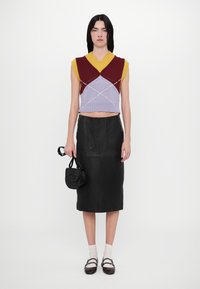 Strikket vest i maroon, lilla og sennepsgul med v-hals og geometriske mønstre, kombinert med et svart skinn blyantskjørt og svart håndveske.