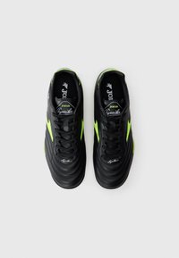 Par de chuteiras pretas e verde néon com atacadores, com a marca "Joma Aguila" no dorso e na biqueira, expostas sobre um fundo branco liso.