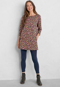 Haljina s uzorkom, okruglim izrezom, rukavima do tri četvrtine i džepovima. Boje uključuju ružičastu, zelenu i žutu na tamnoj pozadini. Nosena s tamnoplavim tajicama i sivim gležnjačama.