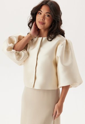 Krem satin cropped bluse med voluminøse puffærmer og en nøglehul-halsslutning, der har en glat tekstur og blød fald.