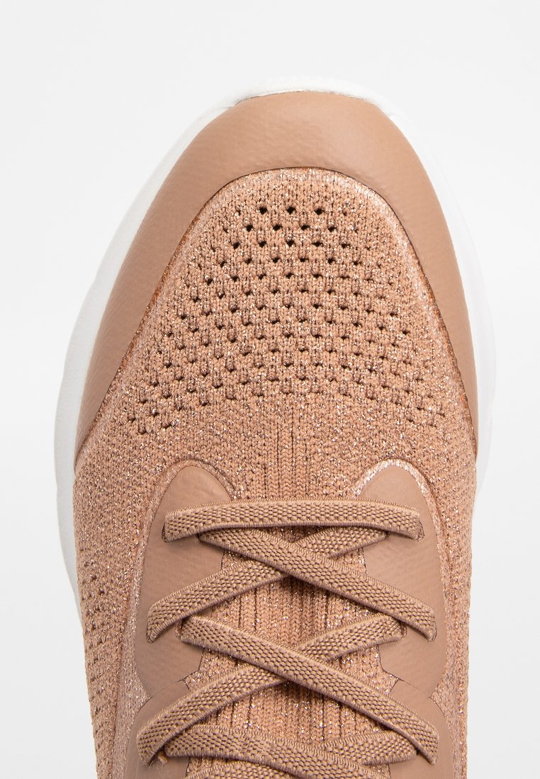 Sportowe sneakersy z teksturowanym, jasnobrązowym siateczkowym wierzchem, okrągłym noskiem i białą gumową podeszwą; cechy obejmują zapięcie na sznurowadła oraz subtelny blask.