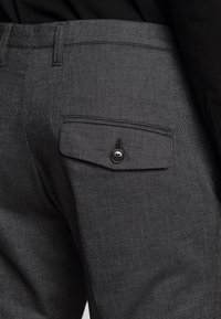 Pantaloni grigi a scacchi con una singola tasca a pattina con chiusura a bottone, tessuto finemente strutturato e vestibilità sartoriale.
