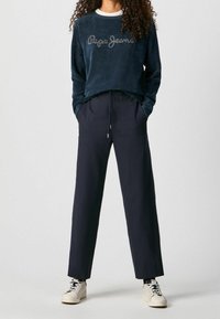 Navy blue fleece sweatshirt with "Pepe Jeans" logo, white collar. Striped navy trousers, elastic waist, paired with white sneakers.