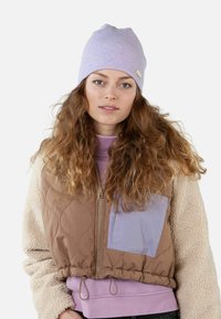 Brown quilted vest with a lilac accent pocket, paired with a light purple beanie and a pastel pink sweatshirt, featuring curly hair.