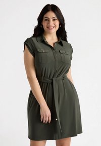 Abito camicia verde oliva con maniche corte, frontale bottonato, due tasche sul petto, vita con cintura e texture del tessuto liscia.