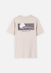 T-shirt en coton beige clair avec un motif graphique de montagnes et d'un soleil en orange et bleu, portant le nom de la marque "Oxbow" en dessous du design.