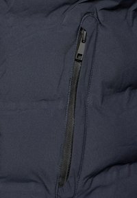 Granatowa kurtka puchowa z elegancką czarną kieszenią na zamek błyskawiczny, wyposażoną w teksturowany uchwyt zamka. Gładkie, matowe wykończenie bez wzorów.