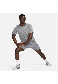 Camiseta deportiva gris y pantalones cortos con el logo de Nike, material ligero, diseño de cuello redondo y silueta ajustada, combinados con calcetines y zapatillas blancas.