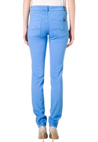 Los jeans ajustados de color azul claro presentan un diseño de tiro medio, dos bolsillos traseros con costura curva, y se combinan con tacones en tonos neutros.