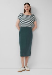 Haut à manches courtes rayé en noir et blanc, associé à une jupe verte ajustée jusqu'aux genoux. Porté avec des baskets blanches avec un accent crème.