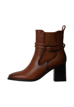 Bottine en cuir marron avec talon bloc, bride latérale avec boucle et clous, et languette à l’arrière.