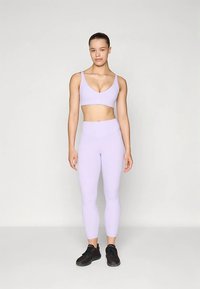 Vaaleanlaventelinvärinen urheiluliivi ja siihen sopivat leggingsit joustavasta materiaalista, joissa istuva malli. Mustat urheilukengät täydentävät asun.