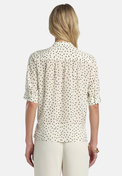 Fehér blúz fekete pöttyökkel, rövid, felhajtott ujjal, hátul vállrész részlettel és enyhén bő fazonnal. Könnyű anyagból készült.