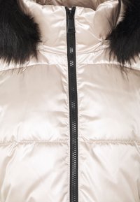 Kurtka puchowa w kolorze kremowym, pikowana, z czarnym zamkiem błyskawicznym i czarnym kołnierzem z sztucznego futra. Gładki, błyszczący materiał z wyściełanymi sekcjami.