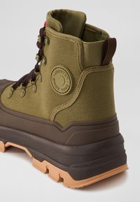Khaki zelené vysoké boty z látky a gumy. Mají kulatý logo, hnědé tkaničky a vzorovanou hnědou a pískovou podrážku pro trakci.
