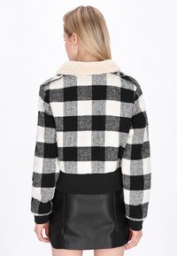 Pullover a scacchi bianco e nero con colletto in pelliccia sintetica, polsini a coste e orlo nero a tinta unita, indossato con una gonna in pelle nera.