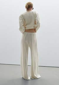 Kremowy zestaw składający się z krótkiej bluzki z długim rękawem i szerokich spodni. Tkanina ma pionowy, żebrowany wzór oraz luźny krój.