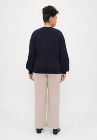 Suéter de malha azul marinho com mangas balão e decote redondo; combinado com calças largas bege e sapatos de salto bloco pretos, visto de costas.