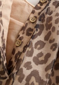 Lähikuva beige-kankaasta, jossa on ruskea leopardikuosi ja kolme pientä beigeä nappia ommeltuna kuviolliseen kangaskappaleeseen.
