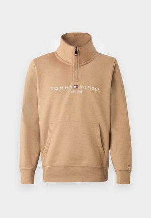 Kreminė užtrauktuku užsegama sportinė striukė su aukštu apykakle ir priekinėmis kišenėmis, ant krūtinės spausdinta "TOMMY HILFIGER EST. 1985".