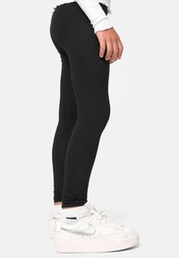 Leggings noirs en tissu extensible, au design ajusté. Associés à des baskets blanches avec des accents argentés et une semelle texturée.