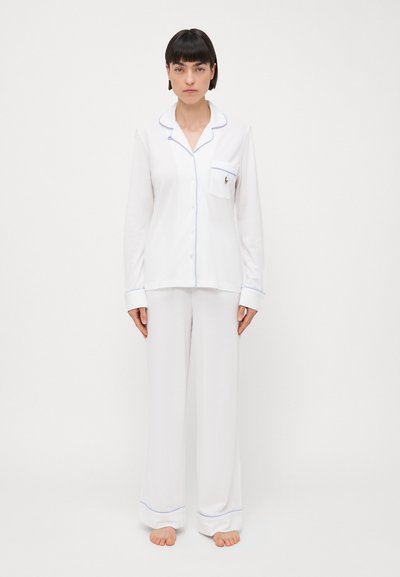 Set de pijamale alb realizat dintr-un material moale, având mâneci lungi, o cămașă cu nasturi și un buzunar pe piept, precum și pantaloni cu bordură de culoare albastru deschis.