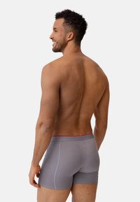 Boxer da uomo grigi con elastico rosso, realizzati in un materiale liscio, con una vestibilità aderente e cuciture piatte per il massimo comfort.